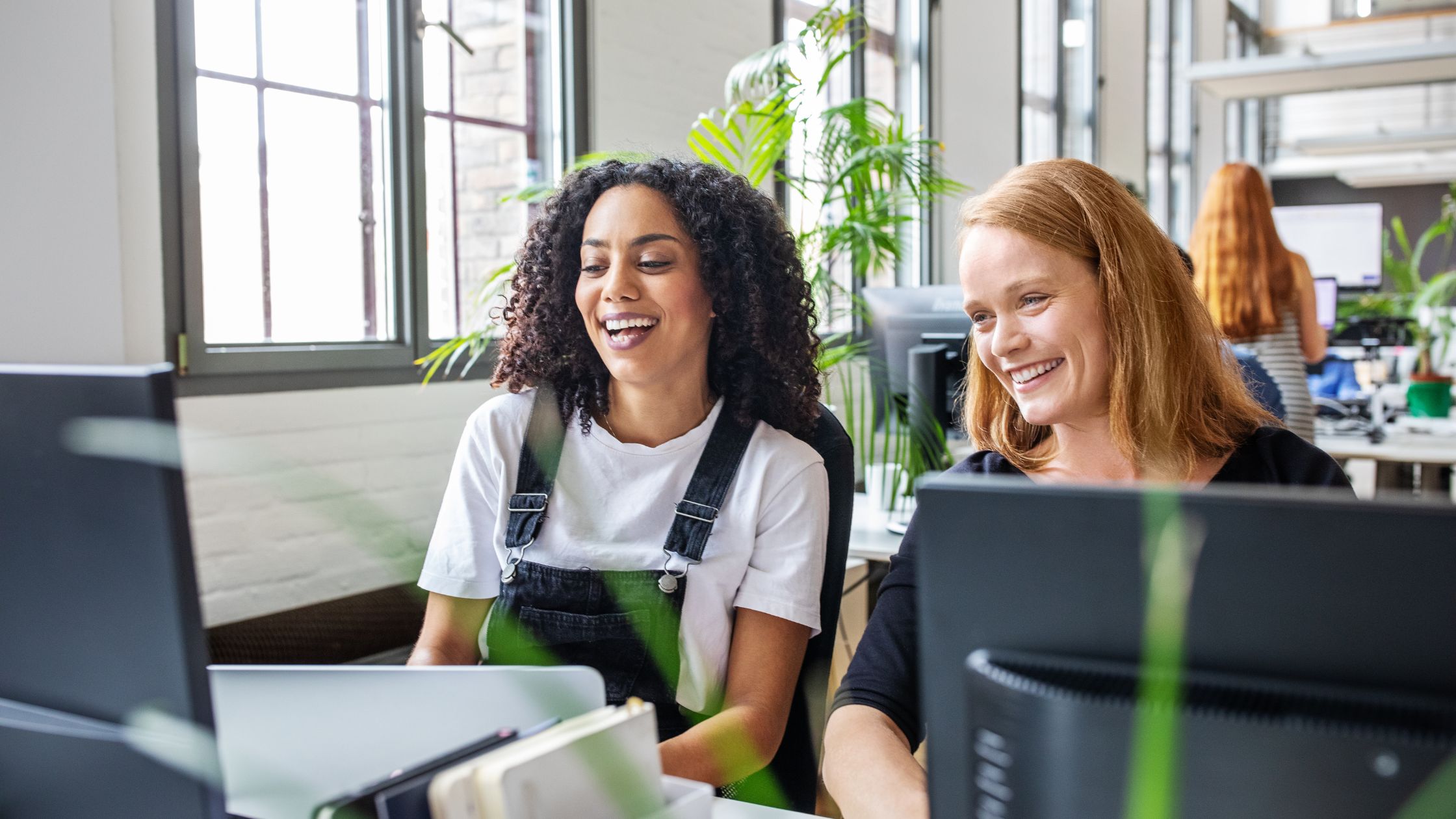 Kaksi naistaLifeworksi ura- ja työelämätutkimus 2023: millä keinoilla uralla pyritään eteenpäin kuvituskuva. hymyilevät toimistotyössä.